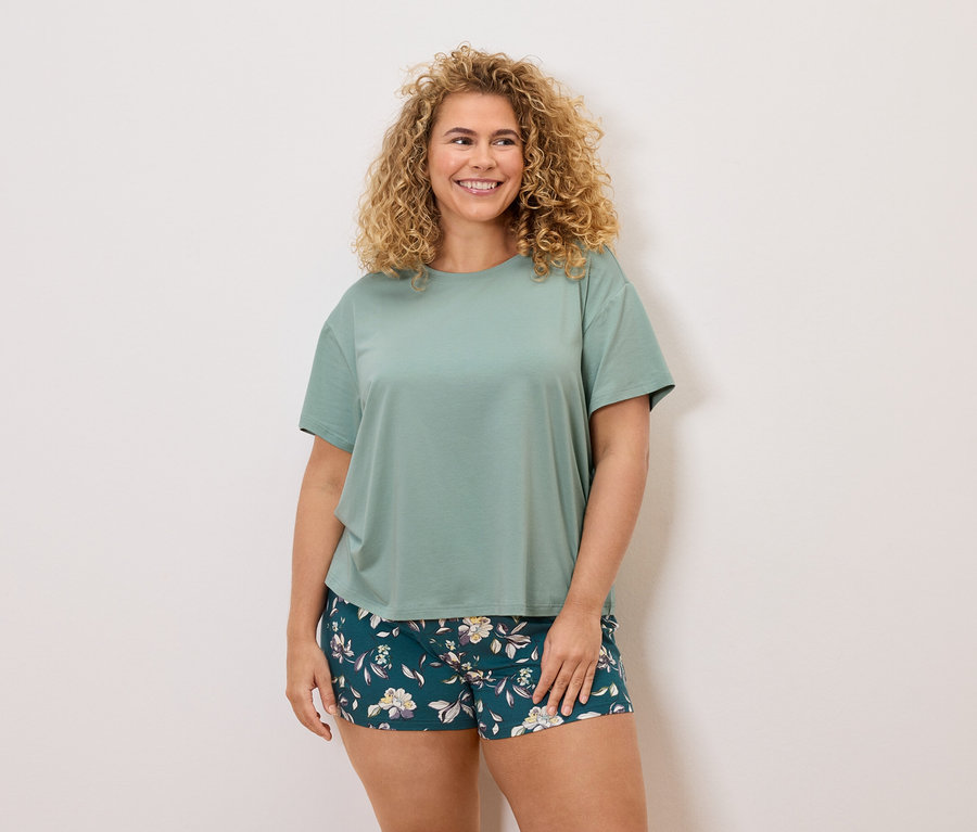 Göndör hajú nő zöld pólóban és virágos rövidnadrágban.