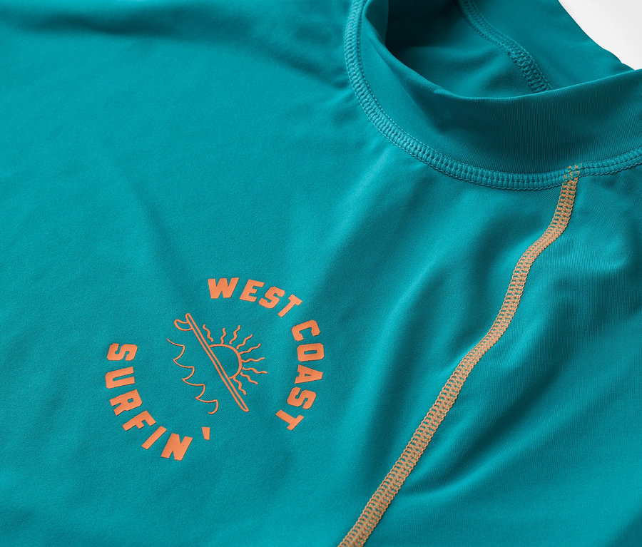 Egy türkizkék, hosszú ujjú póló közeli képe narancssárga "West Coast Surfin" logóval.