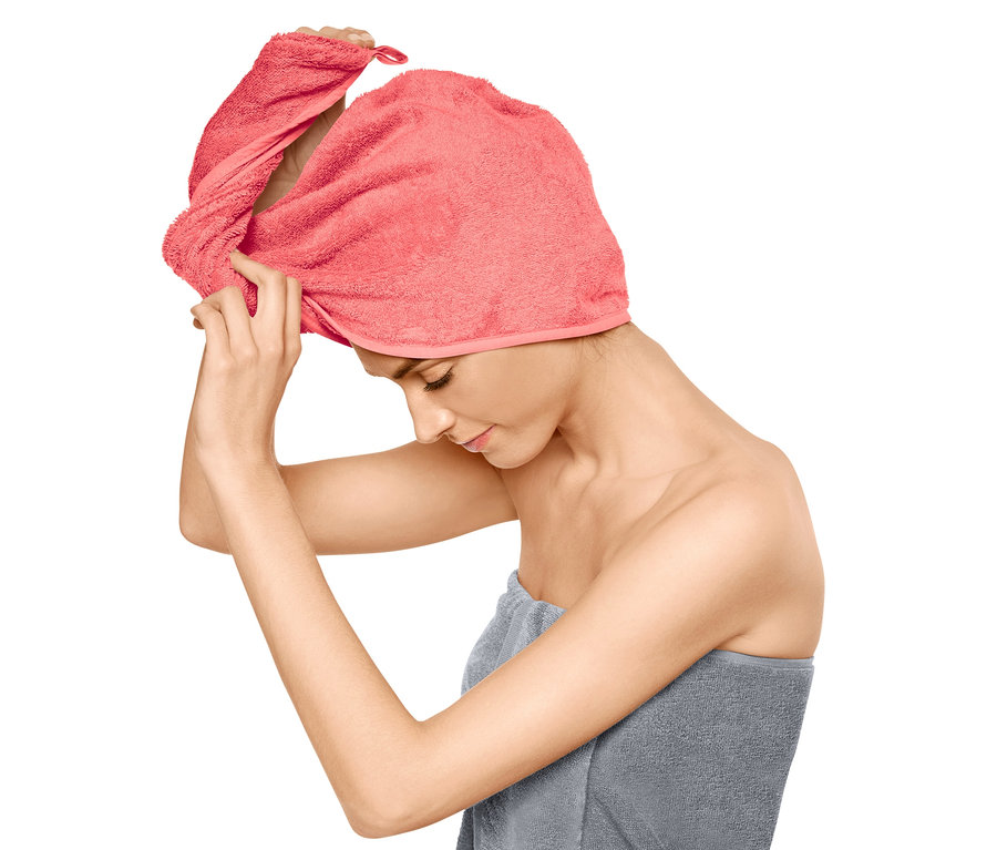 Nő igazgatja a fején a rózsaszín turbán alakú törölközőt, a teste köré szürke törölköző van tekerve.