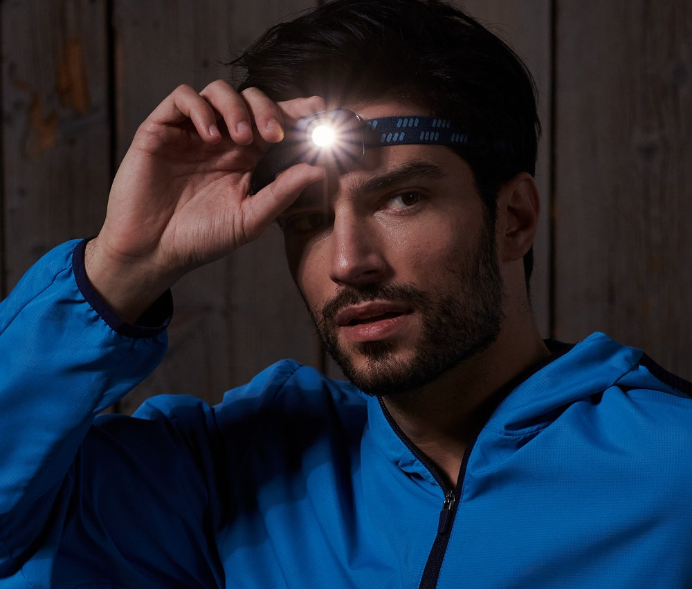 Egy férfi ül egy fa padon és igazgat egy kék LED-es fejlámpát.