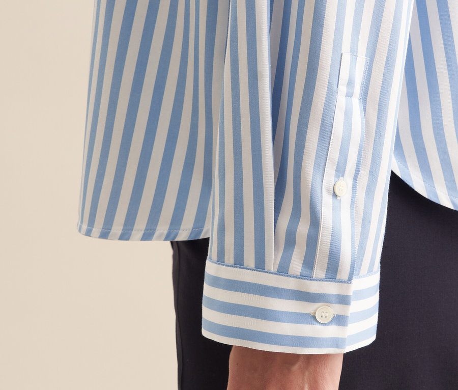 Egy nő karján egy kék, fehér csíkos Seidensticker oversize ingblúz részlete.