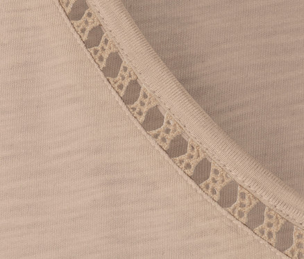 Egy bézs színű pólóblúz részlete horgolt díszítéssel a nyakánál.