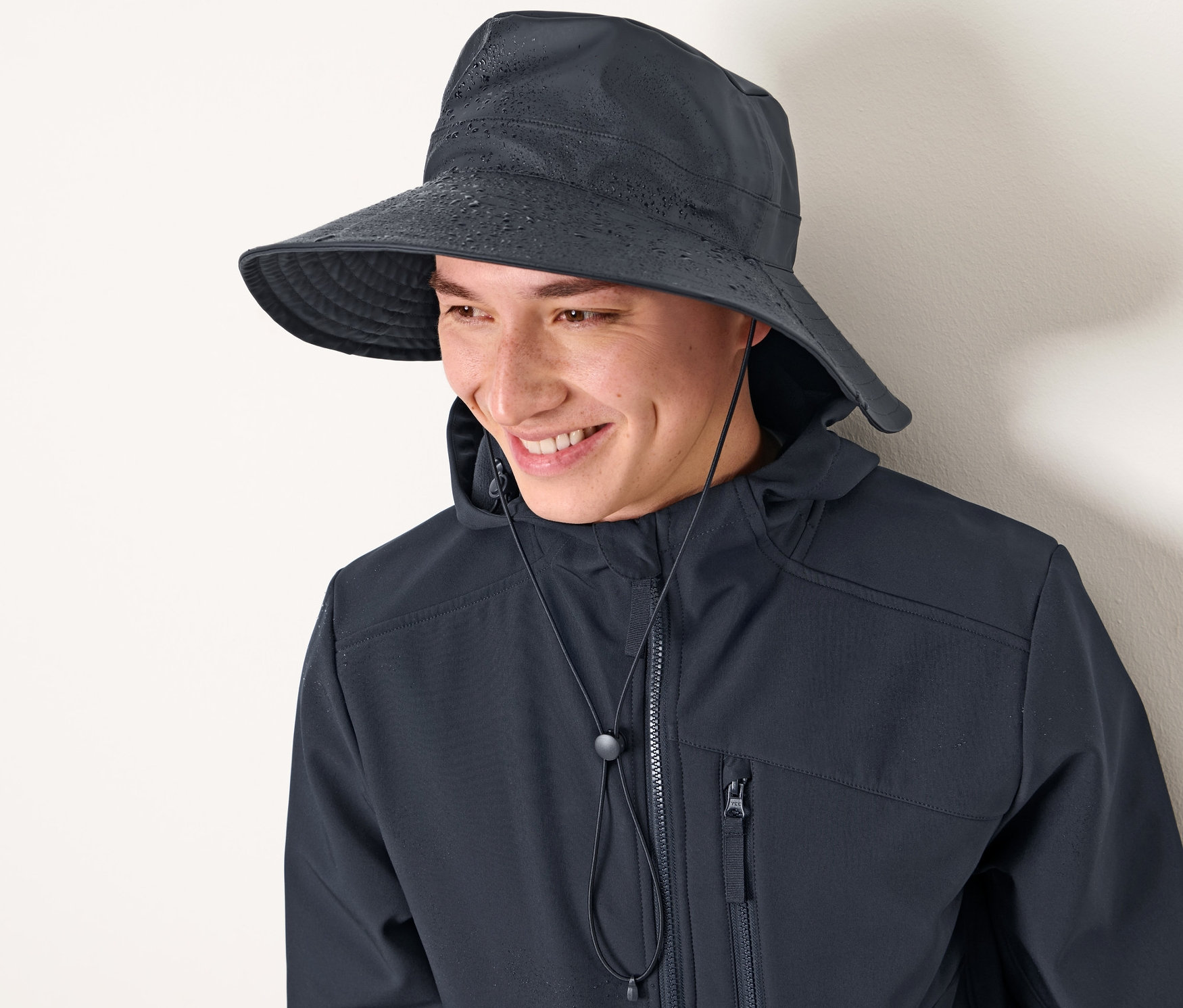 Férfi mosolyog, sötétkék esőkalapot és kabátot visel.