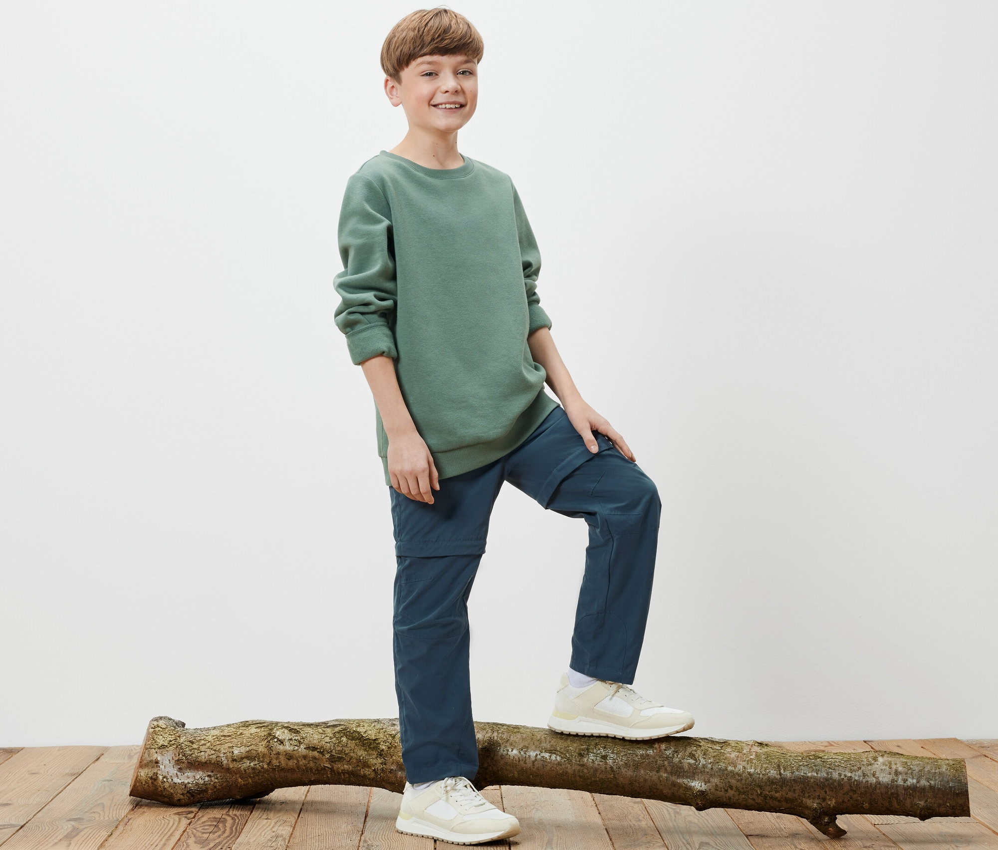 Egy fiú áll egy fatörzsön, és gyerek túranadrágot visel.