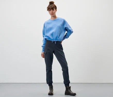 Nő pózol kék pulóverben és tengerészkék softshell futónadrágban.