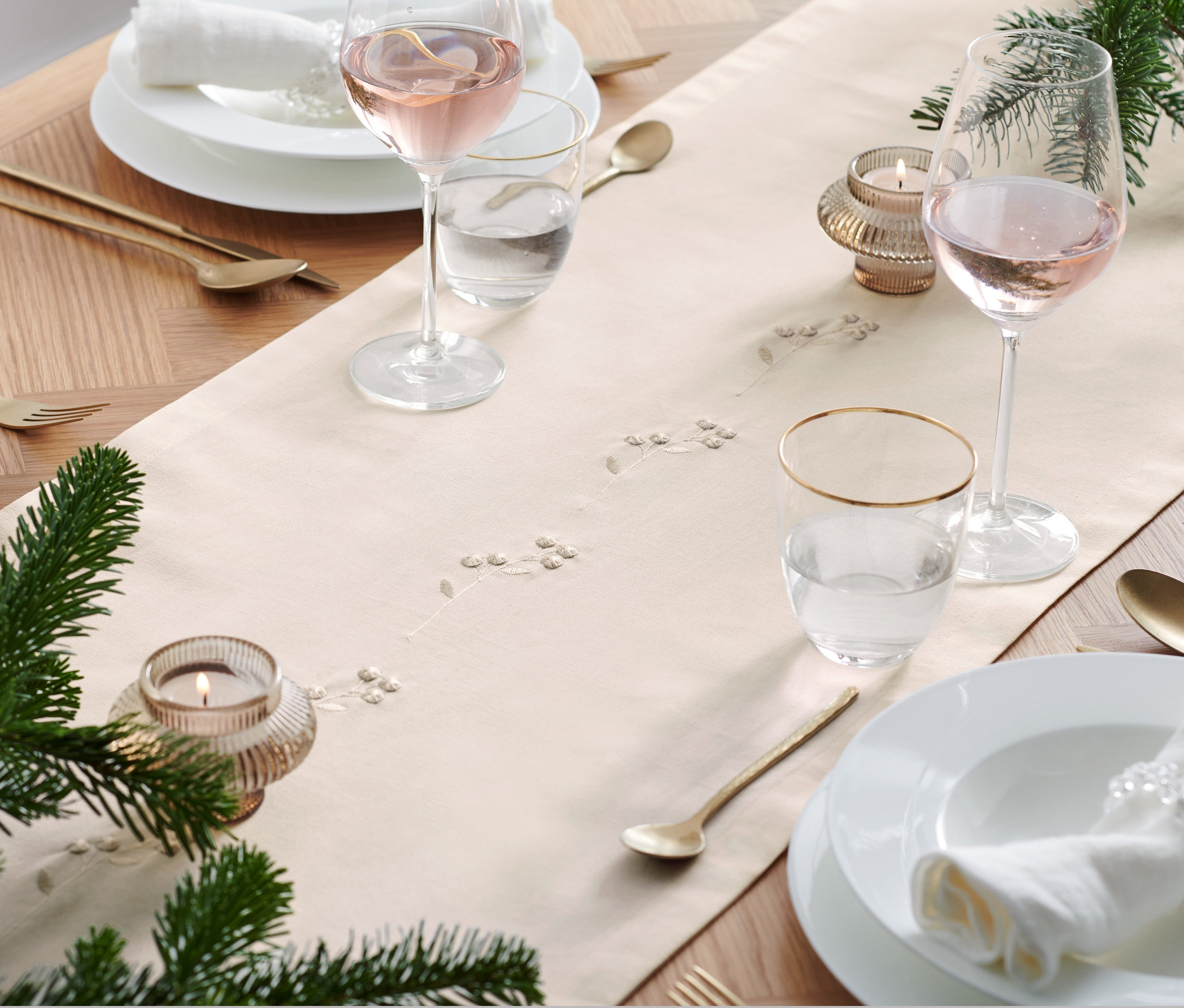 Megterített asztal hímzett asztali futóval, poharakkal, tányérokkal és arany evőeszközökkel.