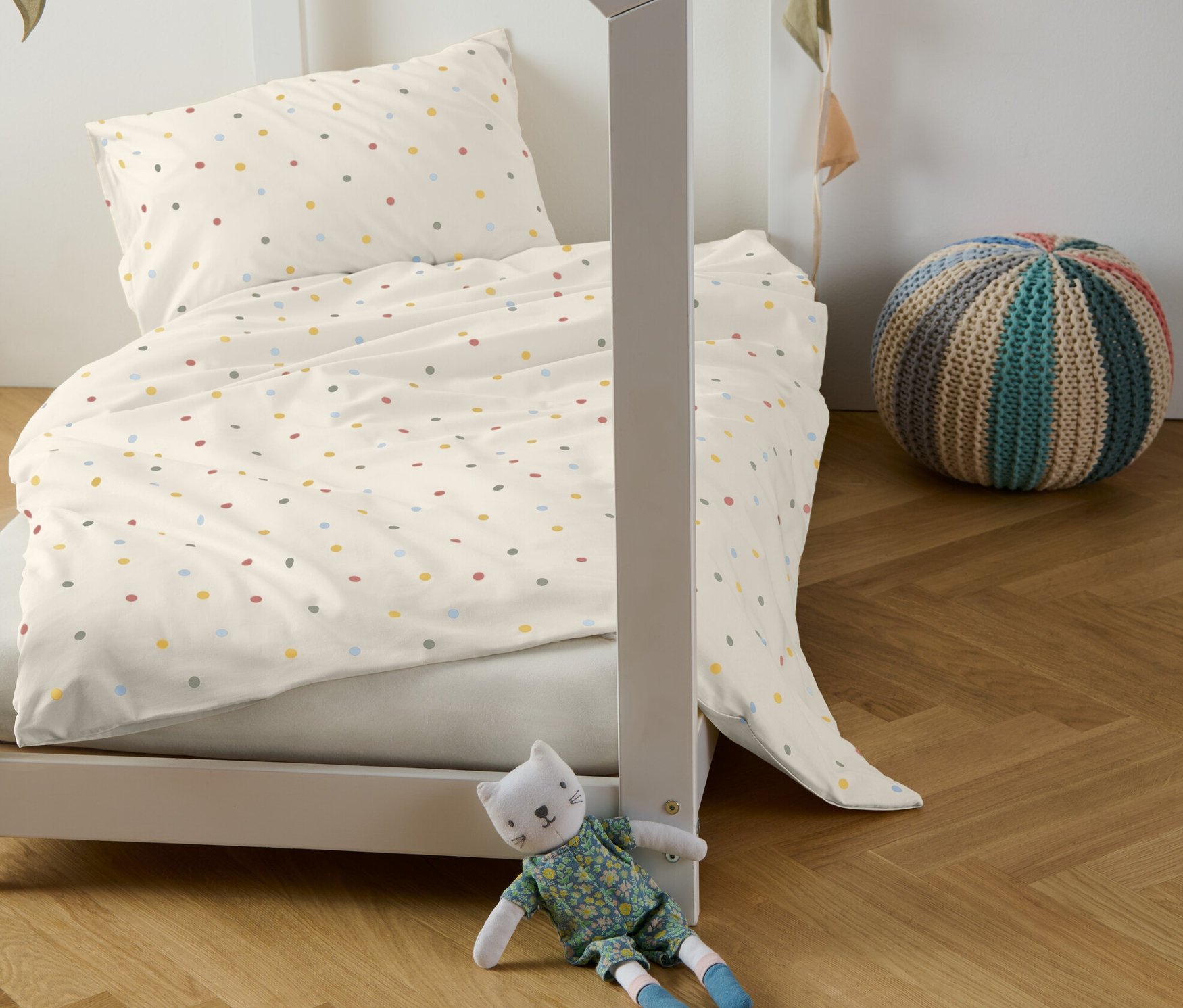 Gyerekágy renforcé gyerekágyneművel, színes pöttyökkel, dekoratív girlanddal és plüss macskával.