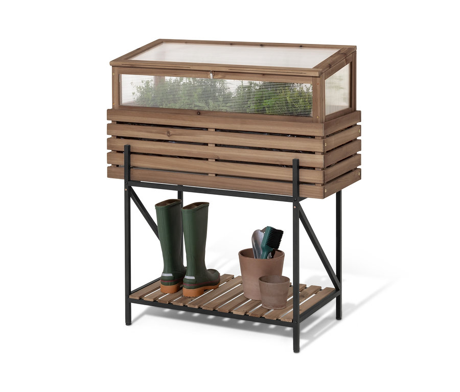 Egy »Elin« magaságyás melegágy fedéllel egy fekete polcon áll. A polcon zöld gumicsizmák és virágcserepek vannak.