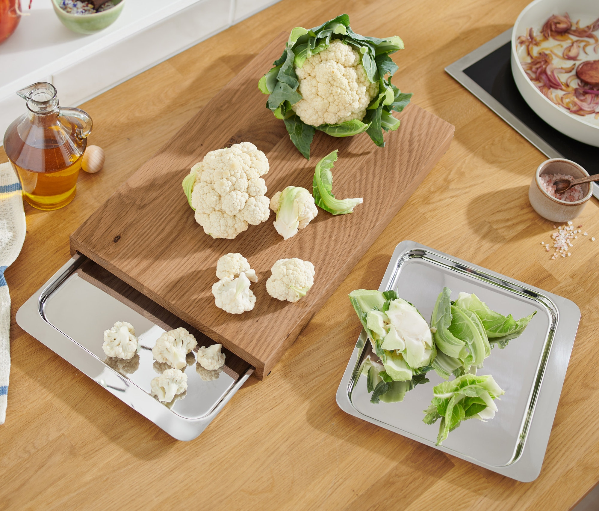Karfiol és vágott darabok vágódeszkán és rozsdamentes acél tálcákon.