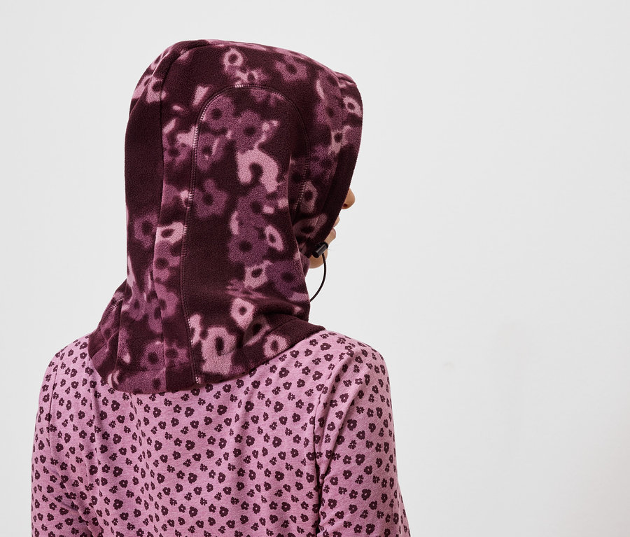 Hátulnézetből egy lila virágos hidzsábot és lila, szívecskés mintázatú inget viselő nő látható.