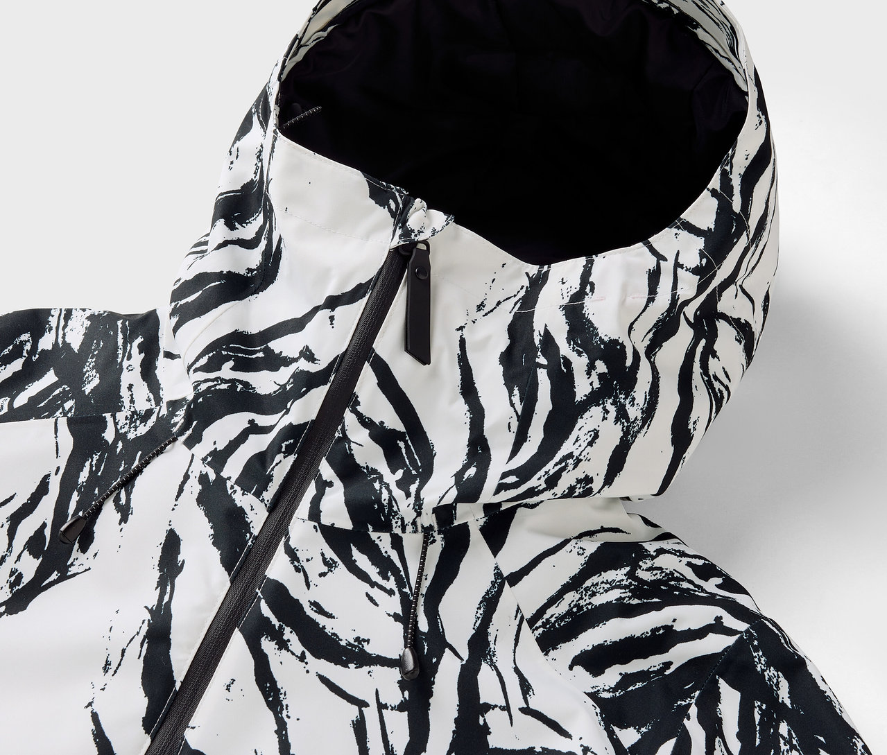 Egy zebra mintás kabát kapucnijának részlete, fekete cipzárral.