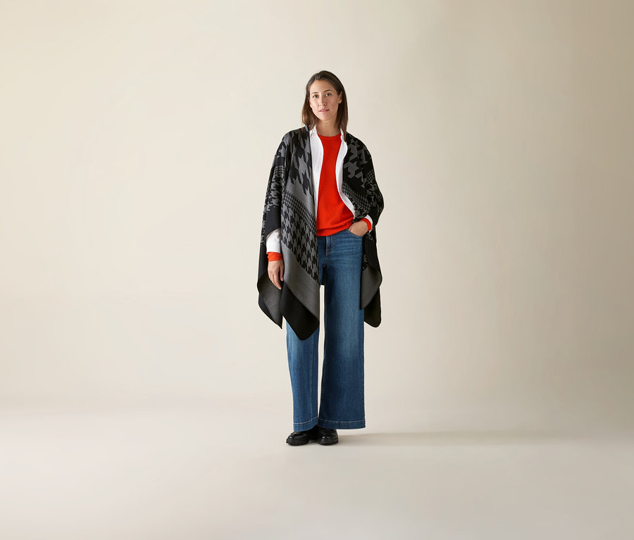 Nő áll, és narancssárga, finom kötésű merinópulóvert visel.