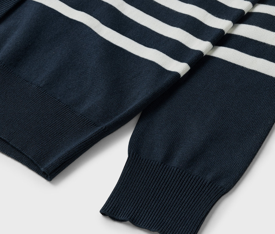 Egy sötétkék, fehér csíkos pulóver részlete, láthatóak az ujjak és a bordázott szegély.