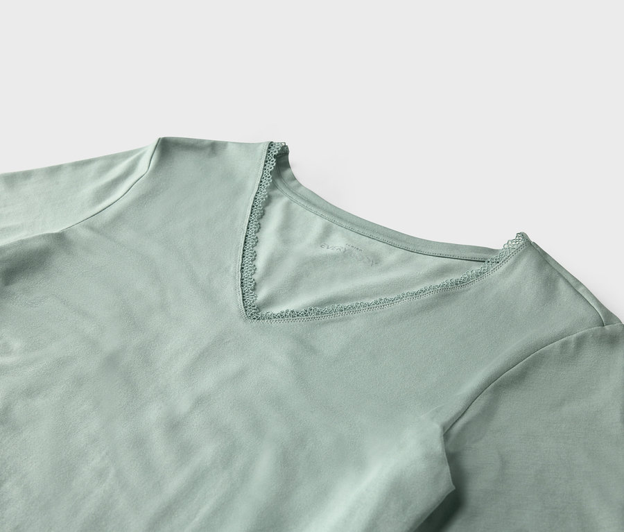 Egy világoszöld, rövid ujjú, csipkével szegélyezett V-nyakú póló részletének közeli képe.