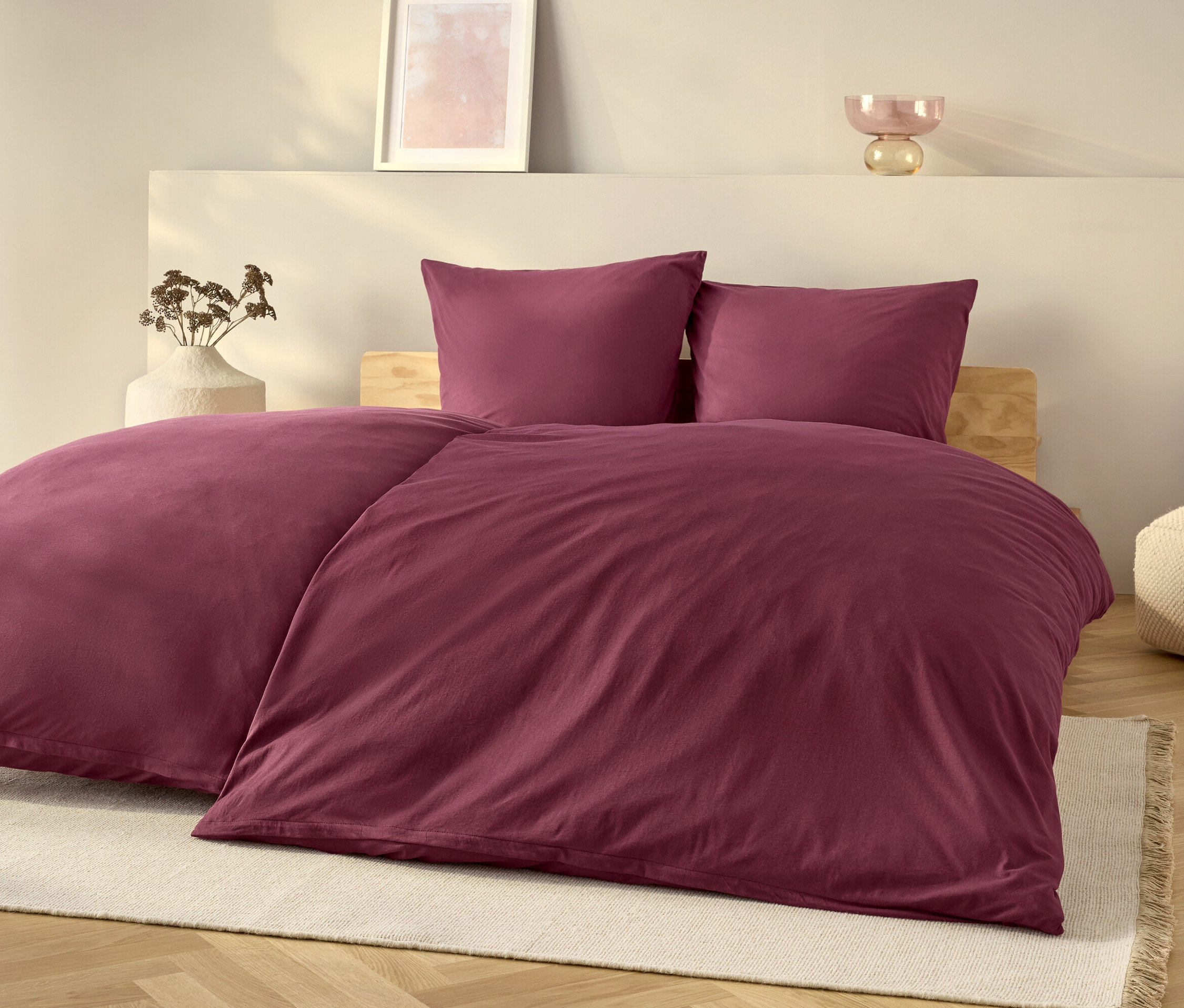 Lila ágynemű szett egy ágyon, fehér szőnyeggel.