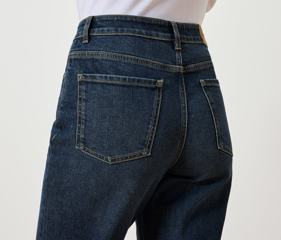 Sötétkék farmernadrág hátsó részletének közeli képe egy személyen, fehér háttér előtt.