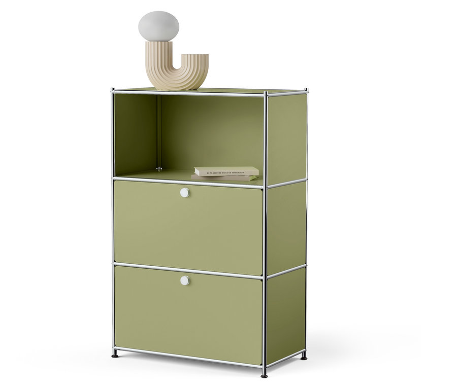 Zöld szekrény két fiókkal és egy nyitott felső polccal, amelyen egy könyv és egy dekoratív lámpa található.