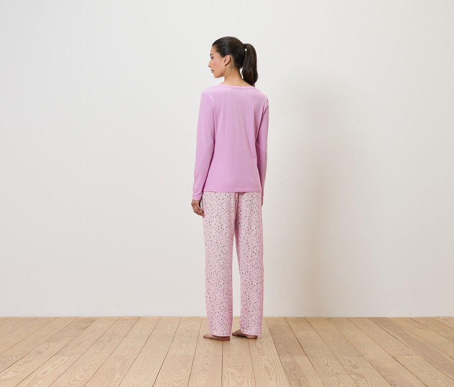 Lila, virágmintás pizsamában álló nő háttal a nézőnek.