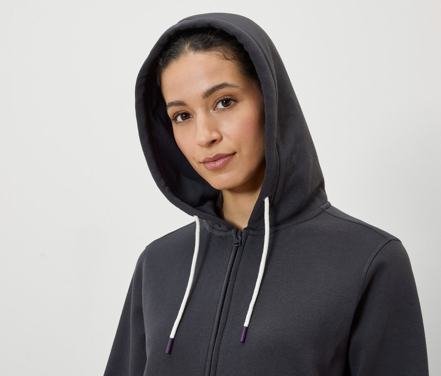 Portré egy kapucnis nőről, aki szürke, cipzáros pulóvert visel, fehér zsinórral.