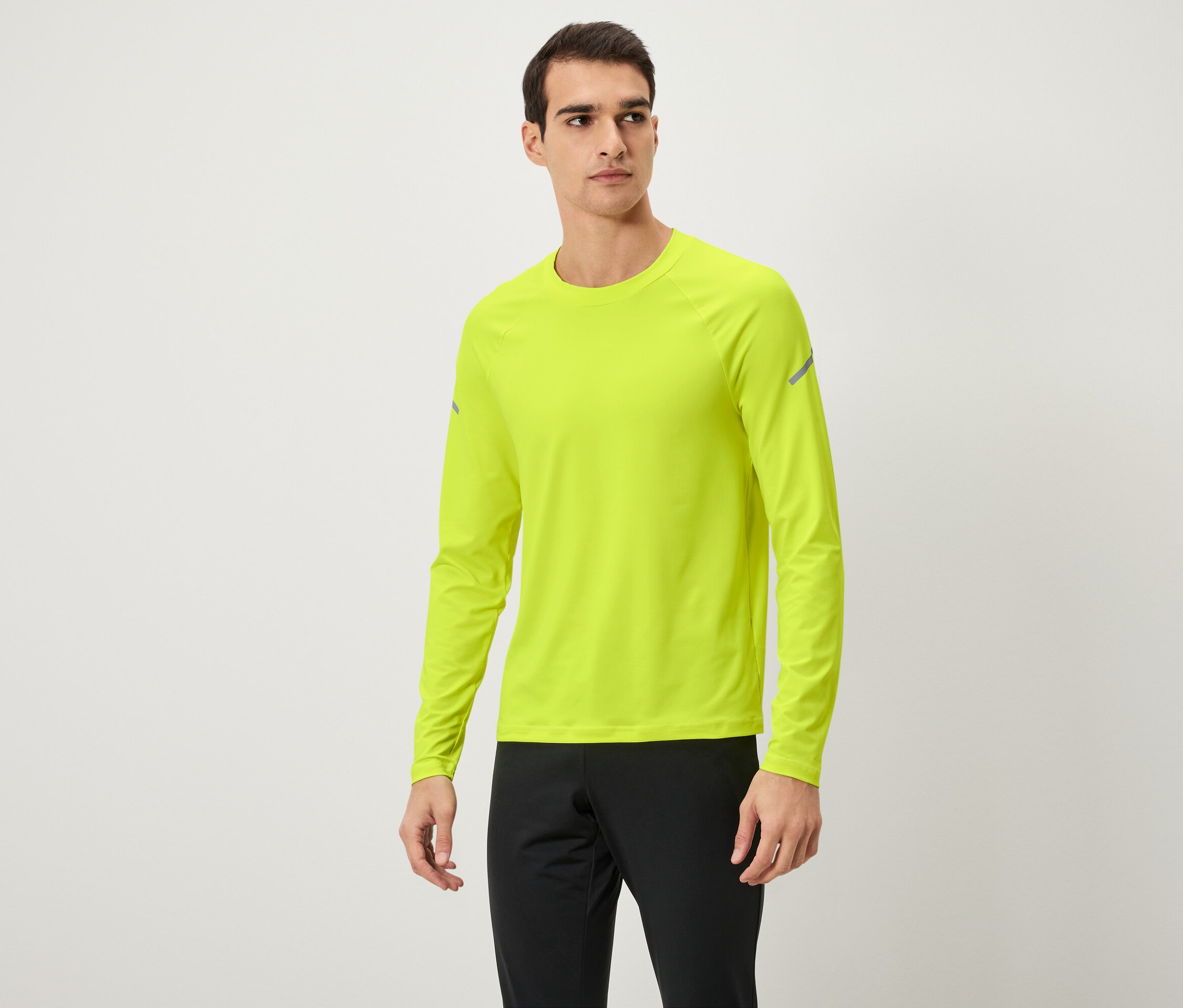 Férfi pózol neon sárga hosszú ujjú pólóban és fekete melegítőnadrágban.