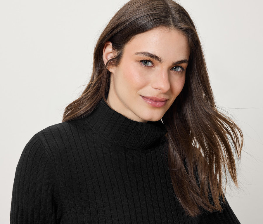 Portré egy mosolygó, hosszú barna hajú nő fekete garbóban.