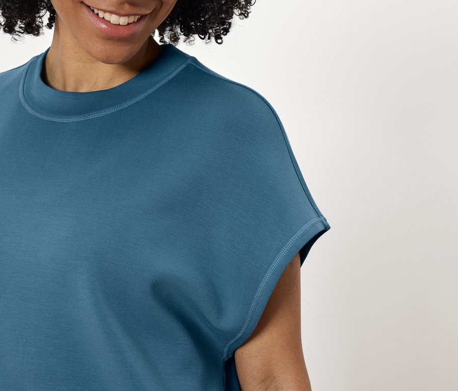 Mosolygó nő kékeszöld pólót visel.