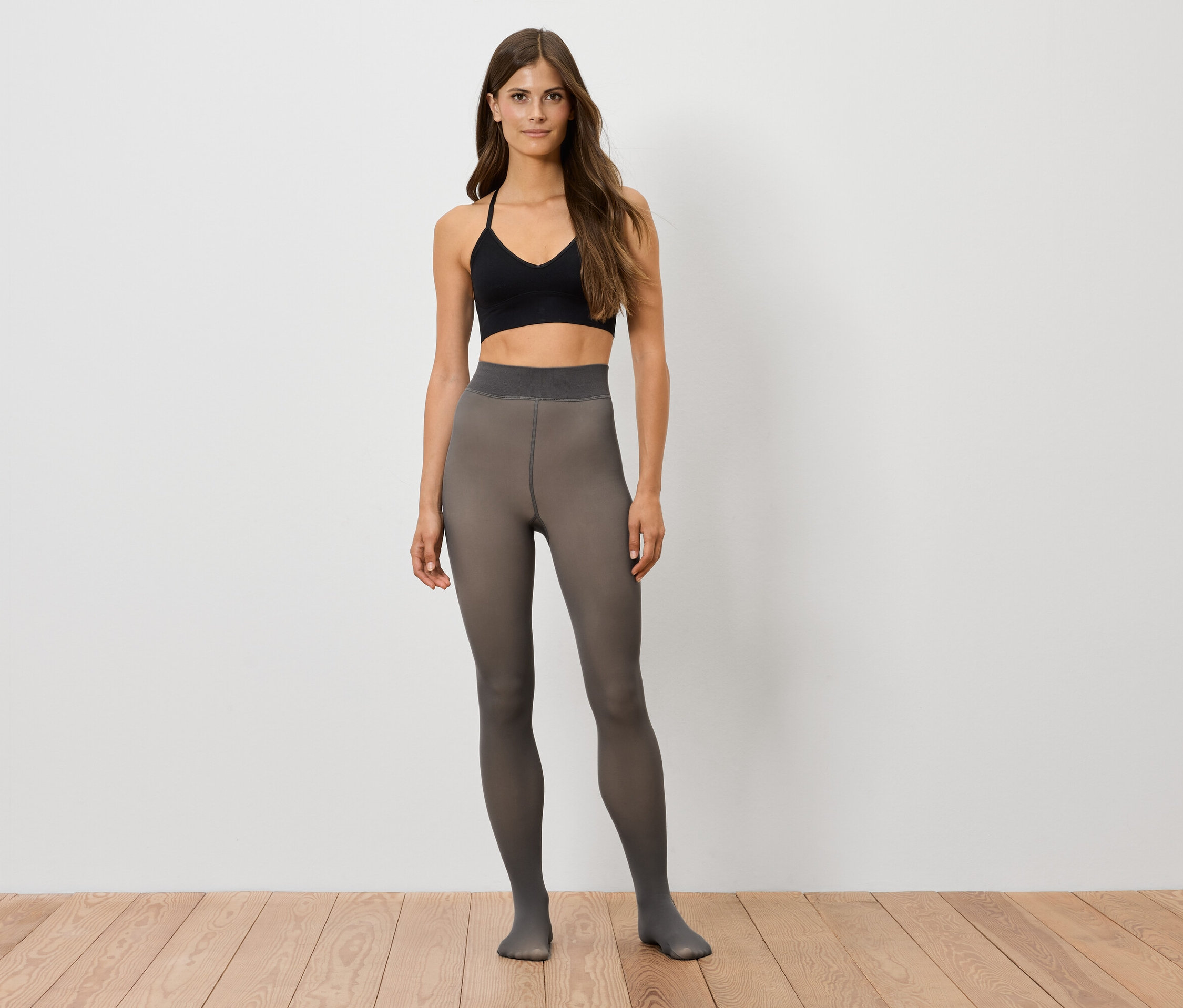 Egy nő áll fekete sportmelltartóban és szürke harisnyában.