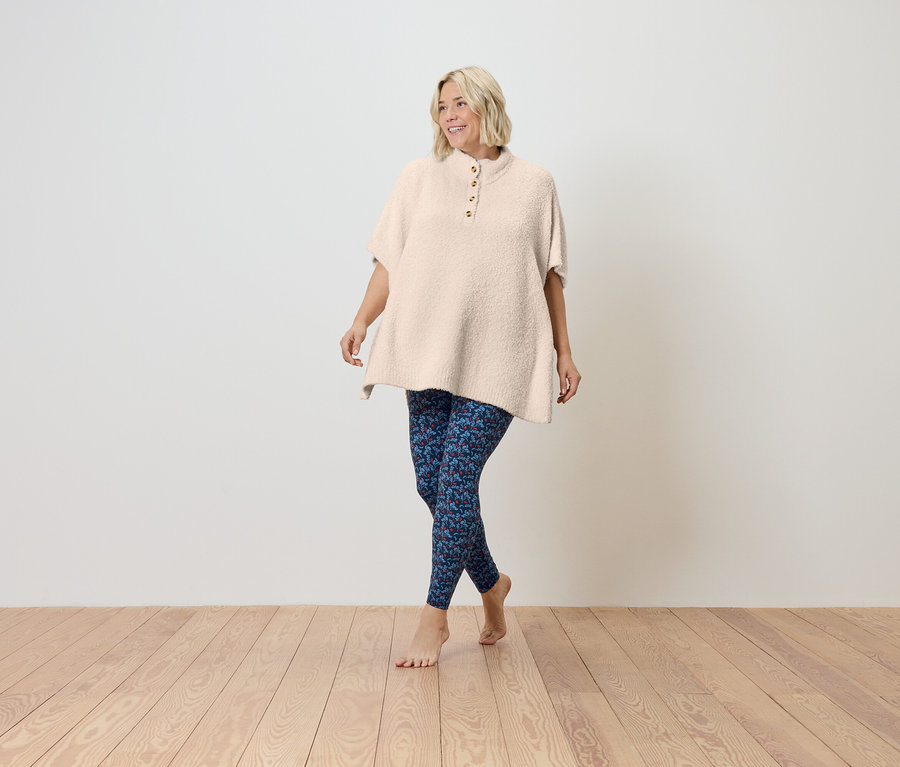 Egy nő mezítláb sétál a fapadlón, rövid ujjú, krémszínű tunikát és kék leggingset visel.