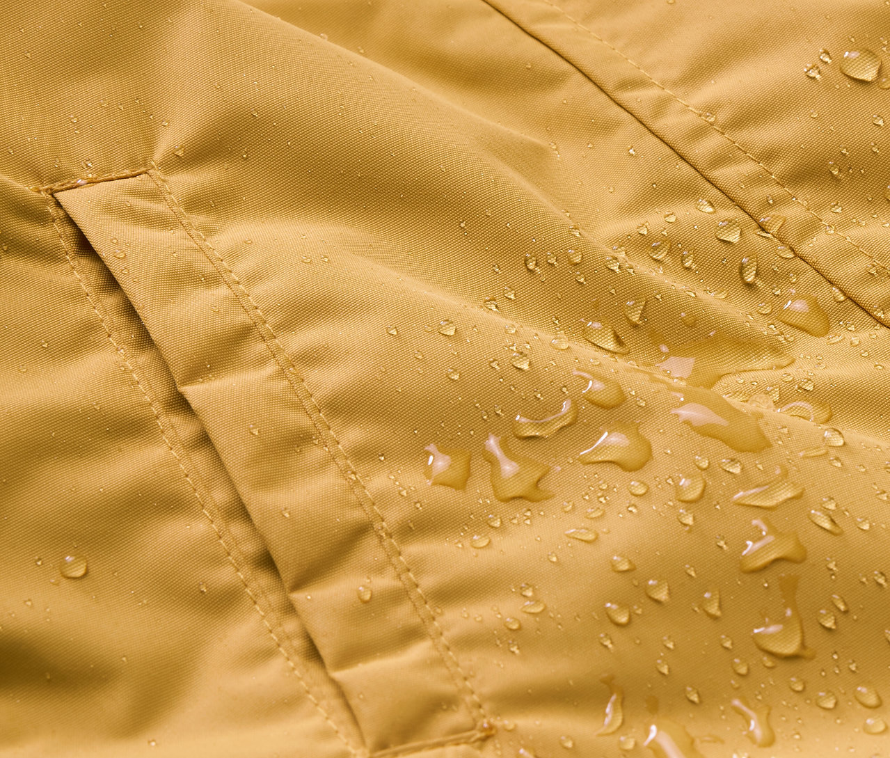 Egy sárga eső elleni kezeslábas részlete, zsebbel és vízcseppekkel.