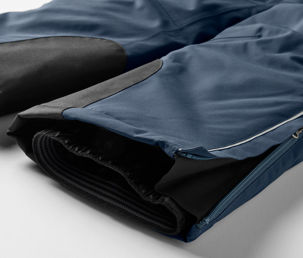 Kék nadrág részlete fekete térdfoltokkal és cipzárral a száron.