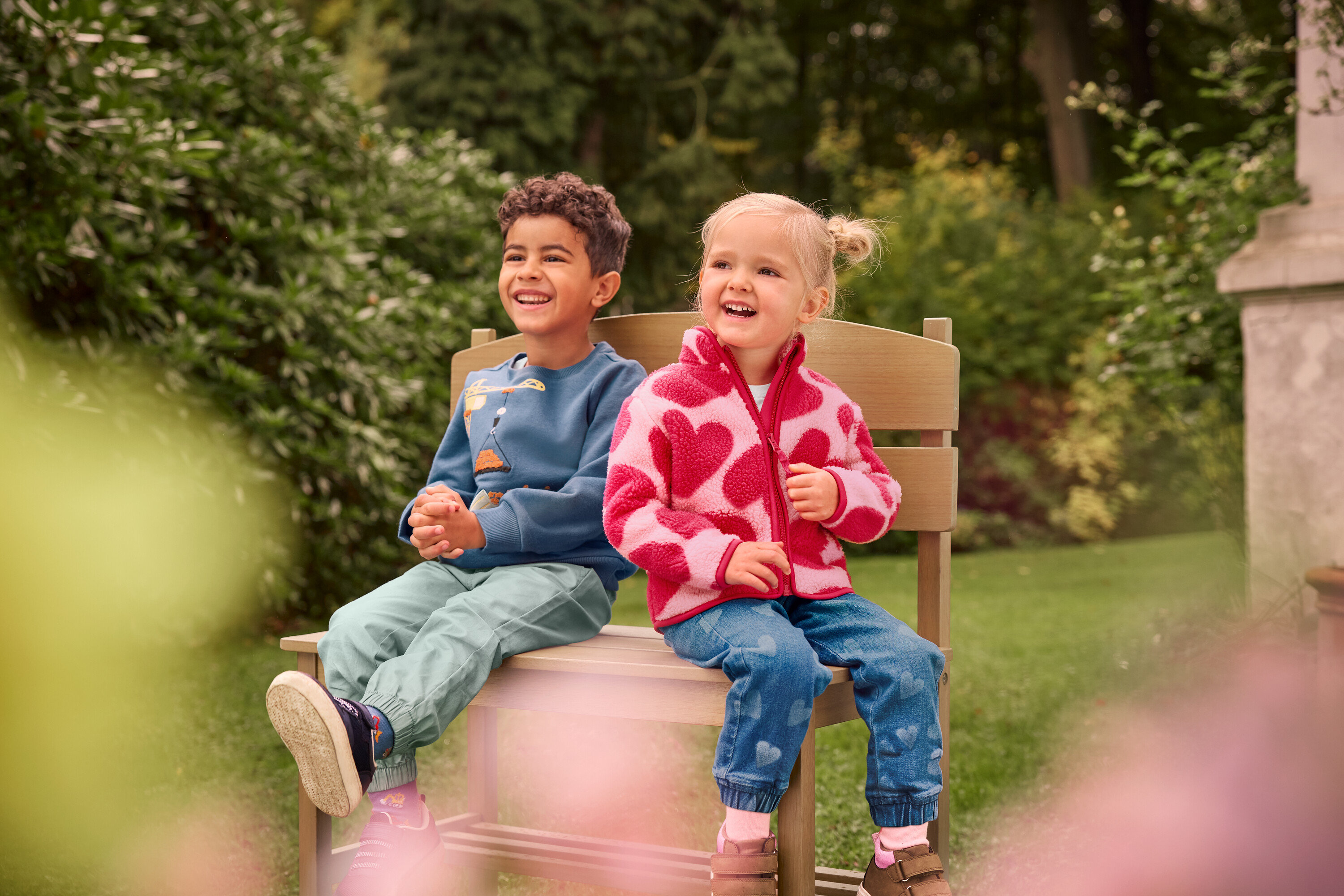 Egy fiú és egy lány ülnek és nevetnek egy kis, polcos kerti padon.