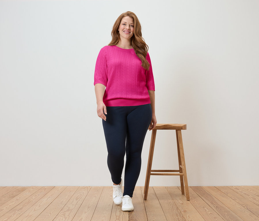 Nő sétál rózsaszín felsőben és sötétkék leggingsben a fapadlón