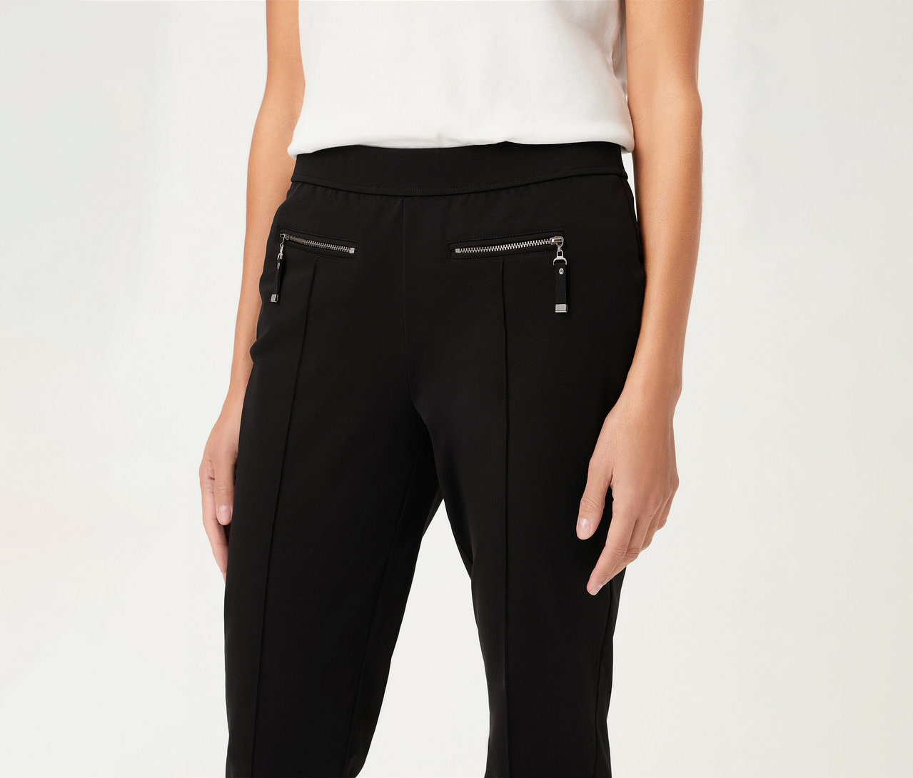 Nő visel egy fekete, szűk Olsen nadrágot cipzárral és egy fehér felsőt.