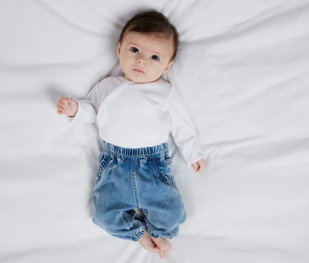 A baba a hátán fekszik, fehér bodyt és NAME IT farmer kisgyerekeknek nadrágot visel.