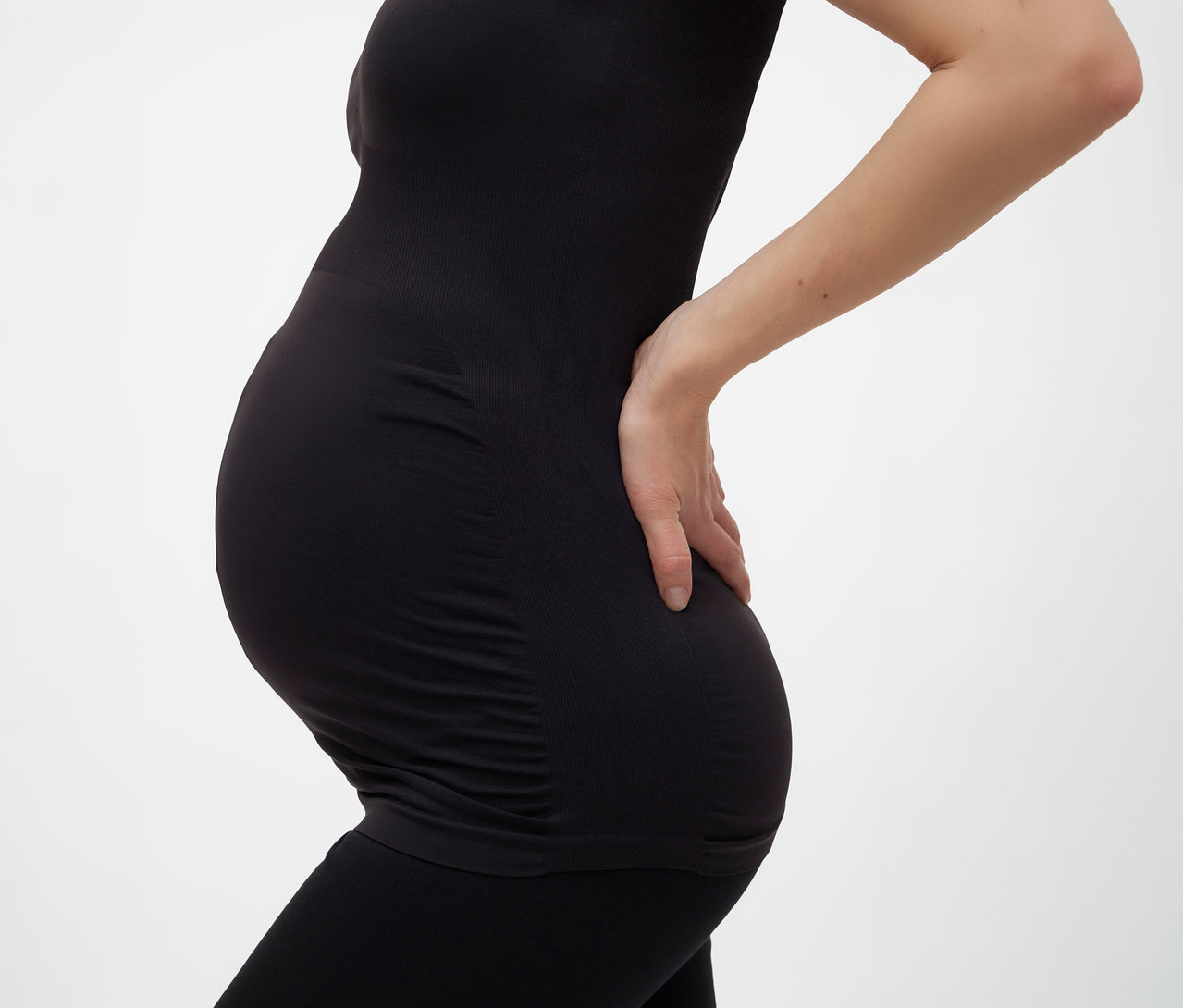 Fekete, egységes méretű MAMALICIOUS kismama topot és leggingset viselő várandós nő, kezével a hátát támasztja.