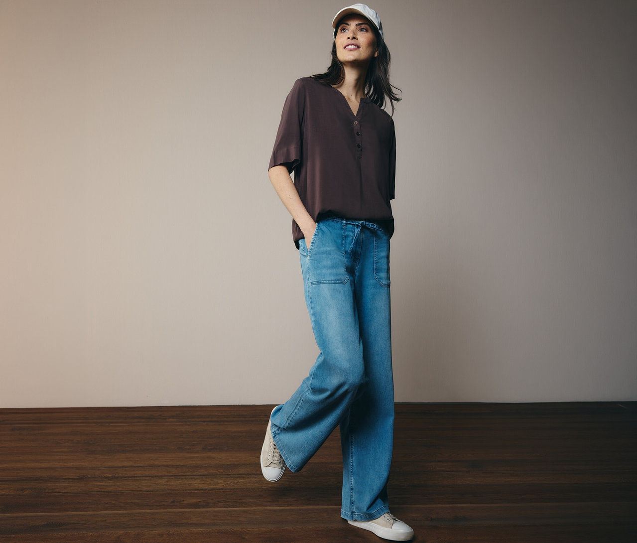 Nő baseballsapkában, barna CECIL tunikablúzban, farmerben és tornacipőben.