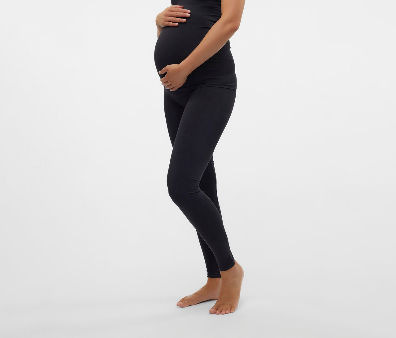 Egy várandós nő a hasát fogja, MAMALICIOUS kismama leggings és egy fekete felső van rajta.