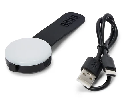 Egy fekete, kerek LED lámpa fekete fogantyúval és egy USB-kábel fekszik egy fehér háttéren.