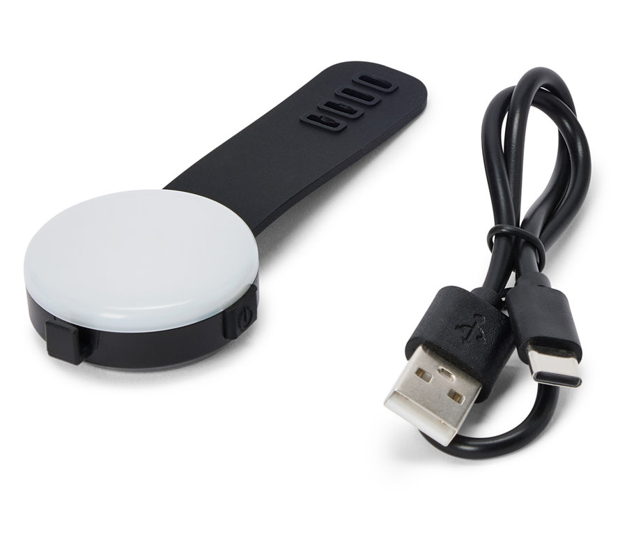 Egy fekete, kerek LED lámpa fekete fogantyúval és egy USB-kábel fekszik egy fehér háttéren.