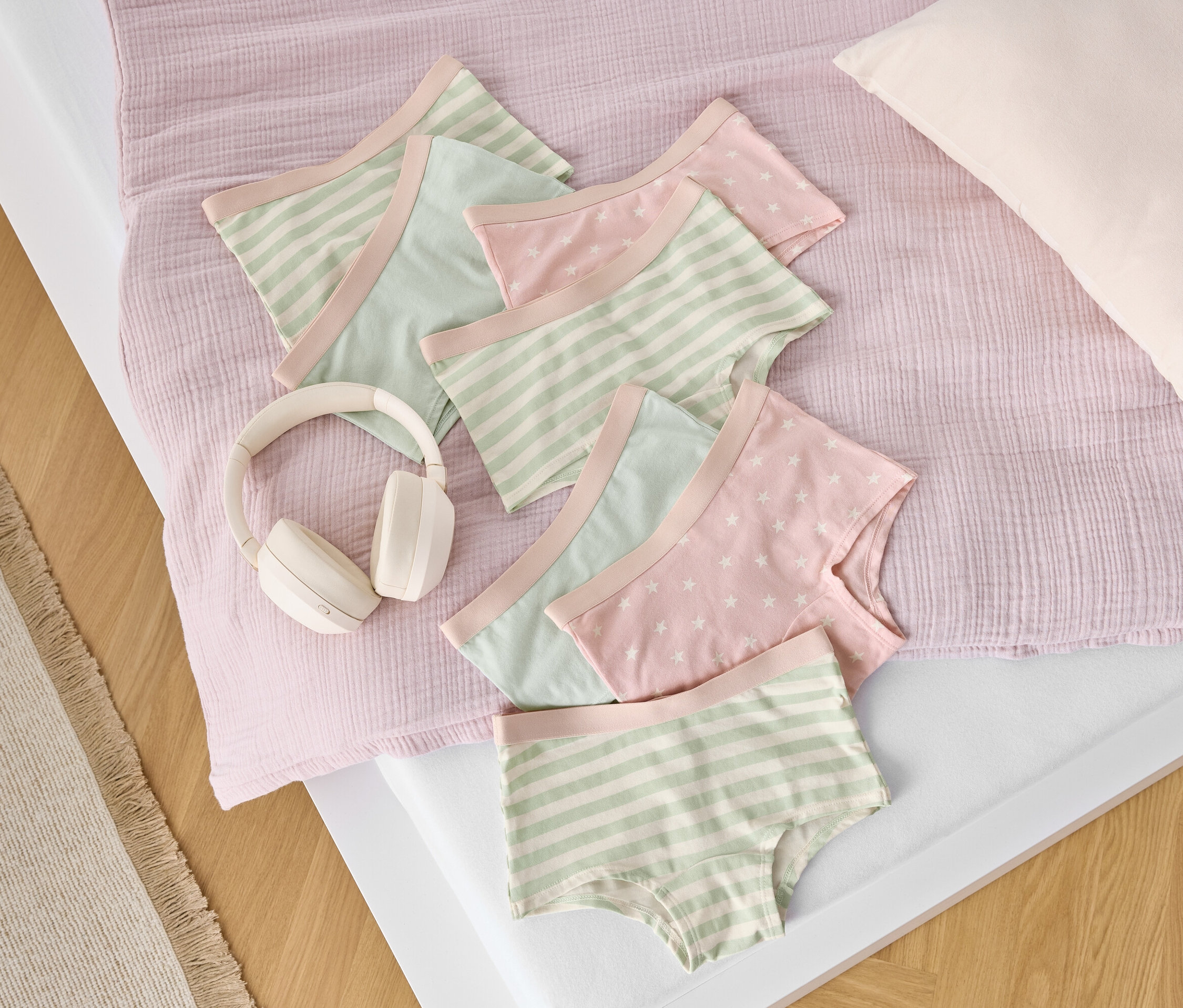 Egy ágyon csíkos és csillagmintás pamut alsónadrágok fekszenek egy fehér fejhallgató mellett.