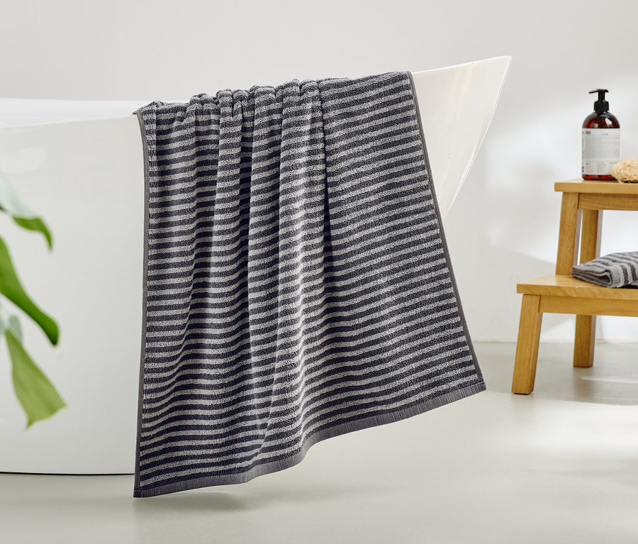 Egy csíkos törölköző lóg a fürdőkád széléről.