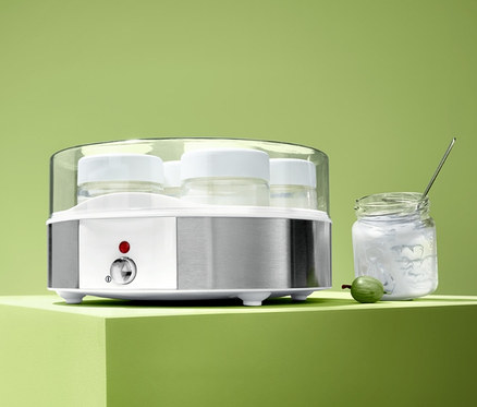 Elektromos joghurtkészítő hét üveggel egy joghurtos üveg és egy zöld köszméte mellett áll.