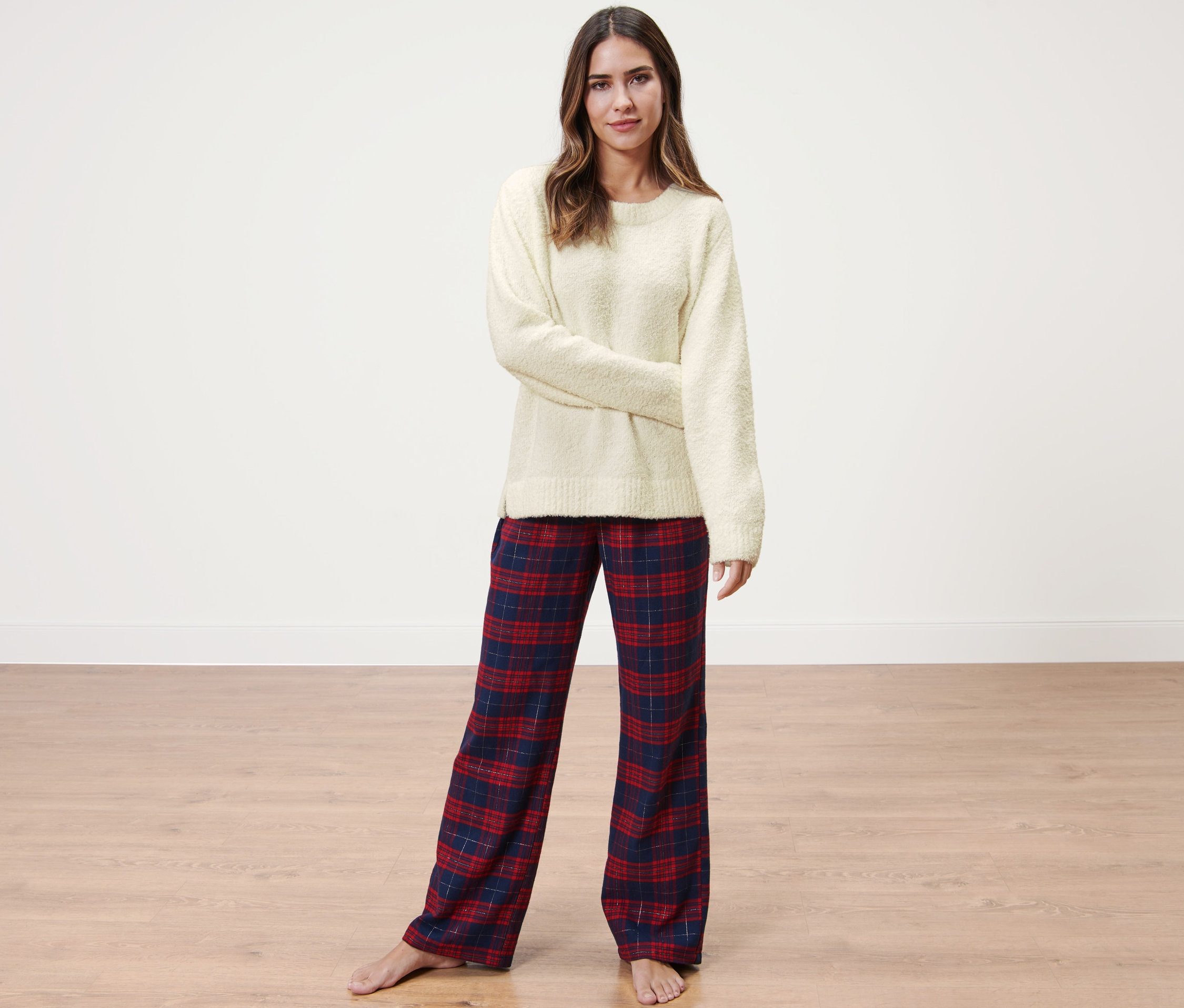 Nő pózol krémszínű plüss pulóverben és kockás nadrágban.