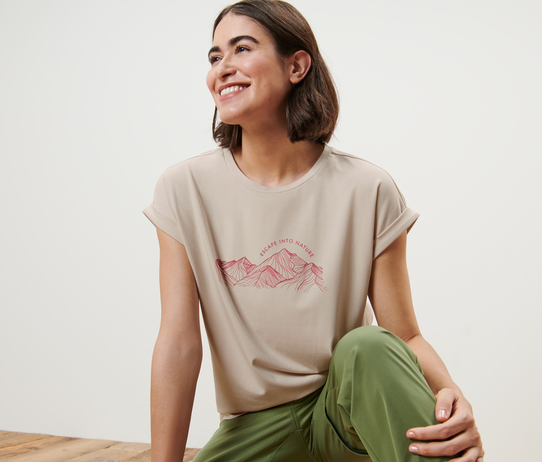 Egy nő ül egy fapadlón, és egy bézs színű, hegyes mintás pólót visel.