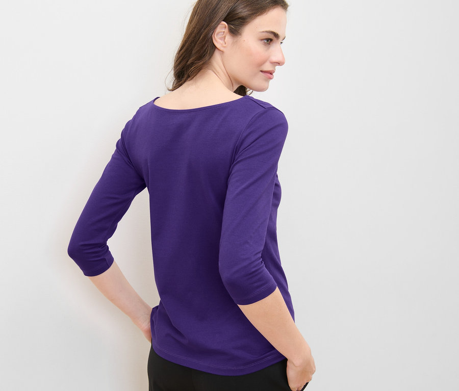 Nő lila, 3/4-es ujjú felsőben pózol.