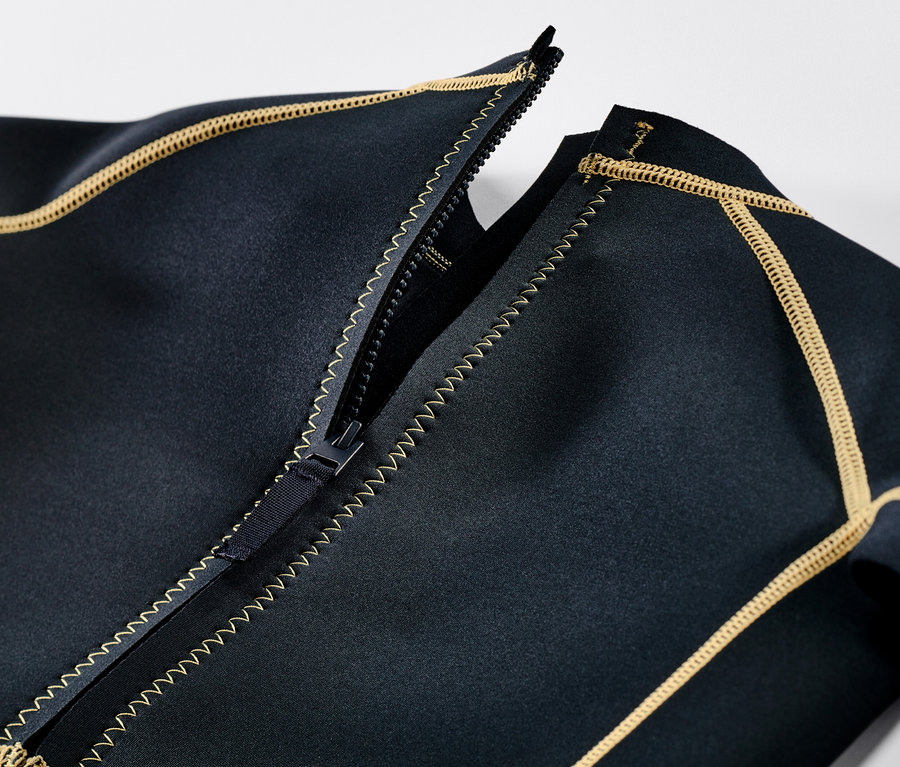 Egy gyerek neoprénruha részlete, nyitott cipzárral és sárga díszvarrással.