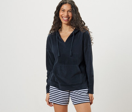 Nő visel sötétkék női kapucnis frottírfelsőt és csíkos rövidnadrágot.