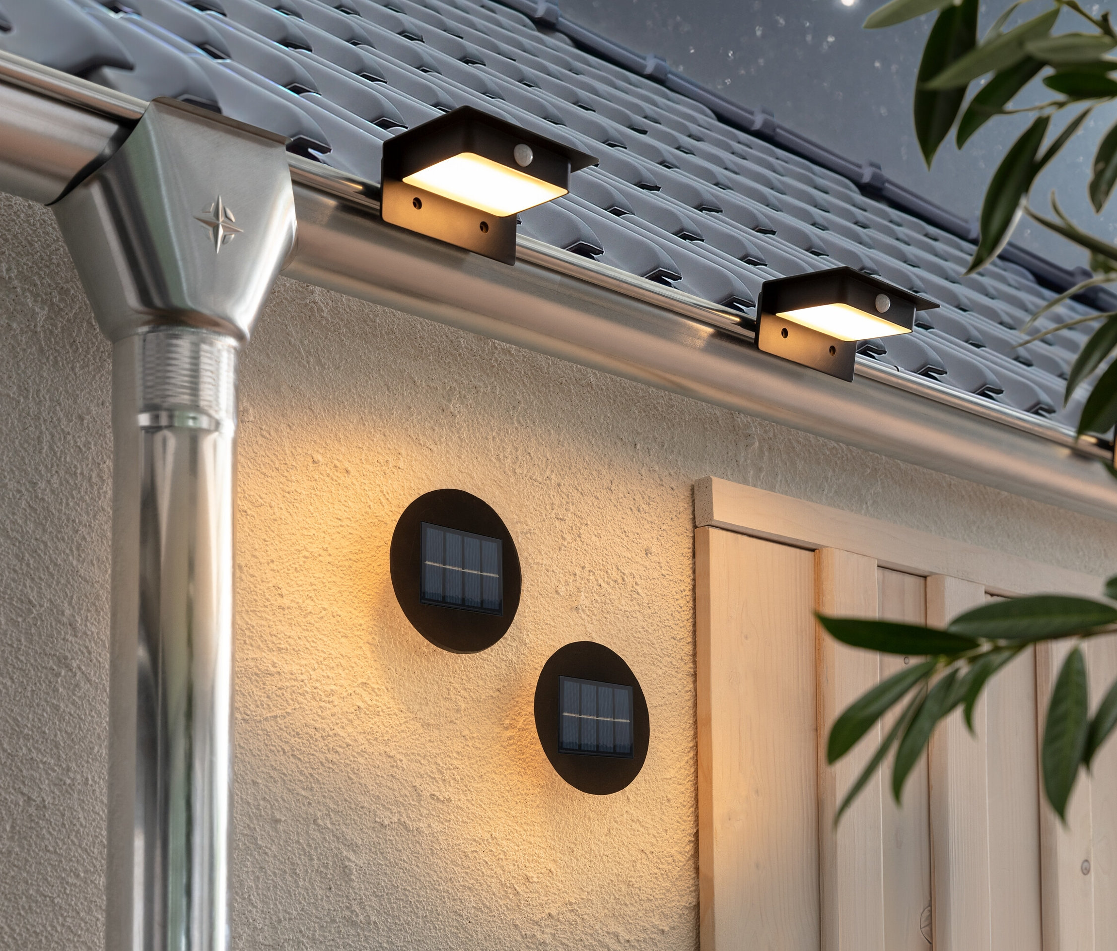 Két napelemes fali és lépcsővilágító lámpa és három napelemes ereszcsatorna-lámpa van rögzítve a ház falán és ereszcsatornáján.