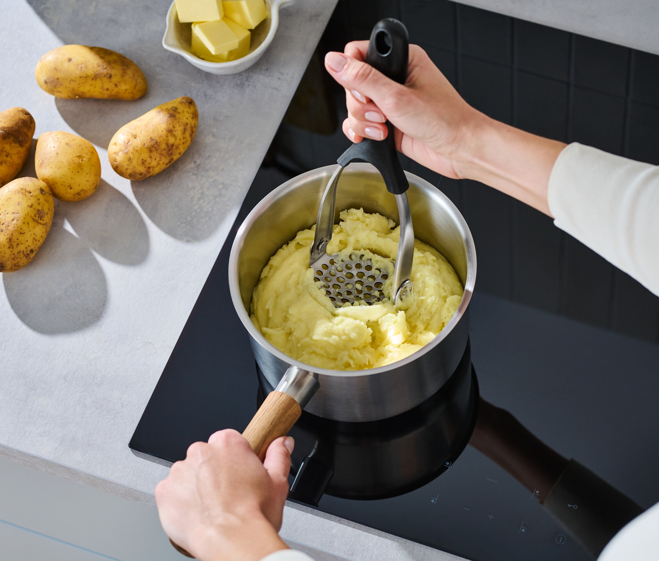 Egy nő összecsukható krumplinyomóval töri a burgonyát egy fazékban a tűzhelyen.