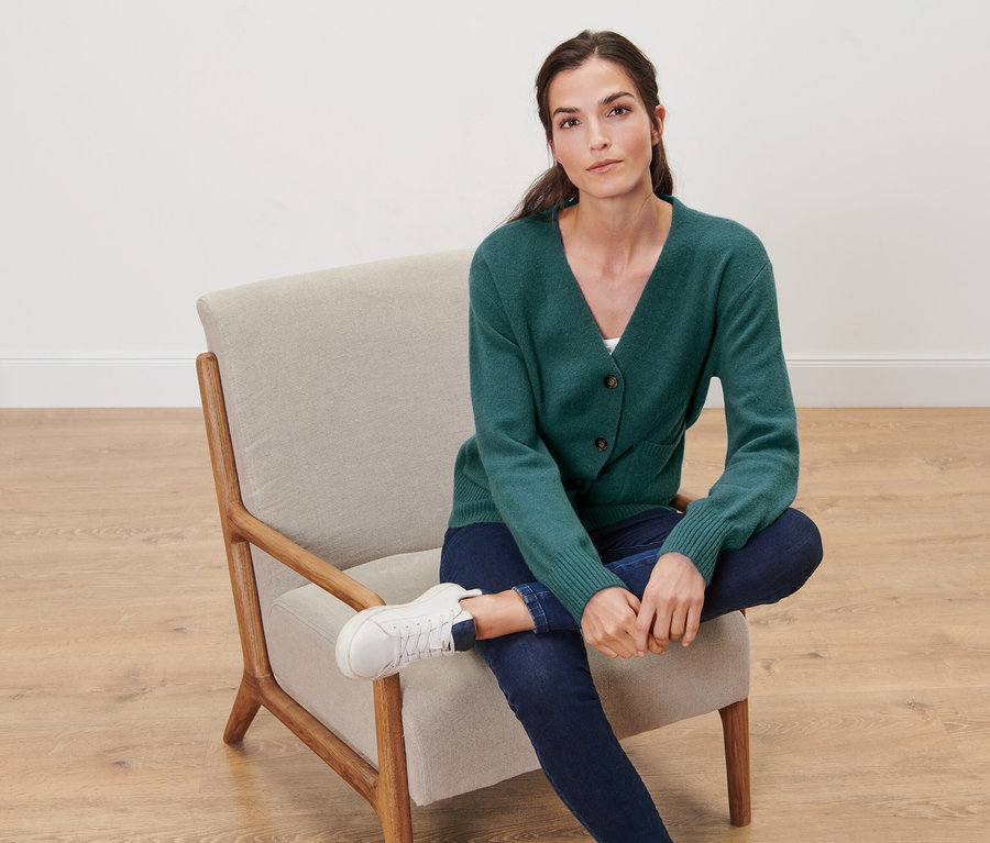 Nő ül egy székben, és sötétzöld, gyapjú kötött kardigánt visel.